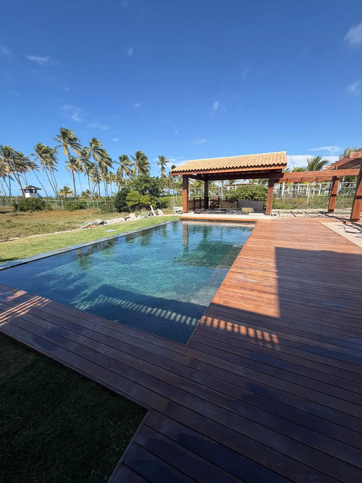 Piscina e pavilhão em madeira diante dos coqueiros